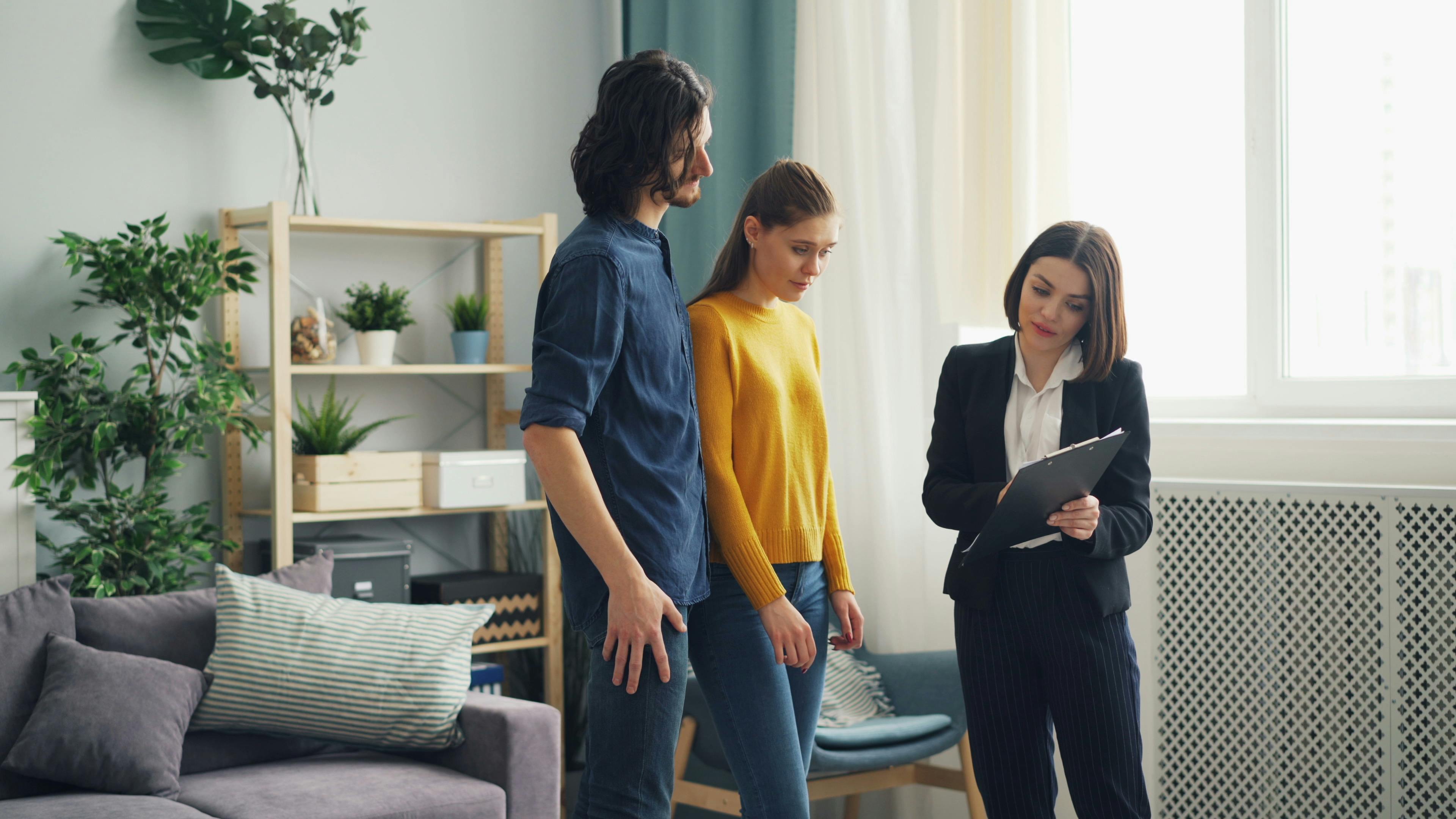 Real estate agent consulting a couple in a modern living room setting, surrounded by indoor plants.