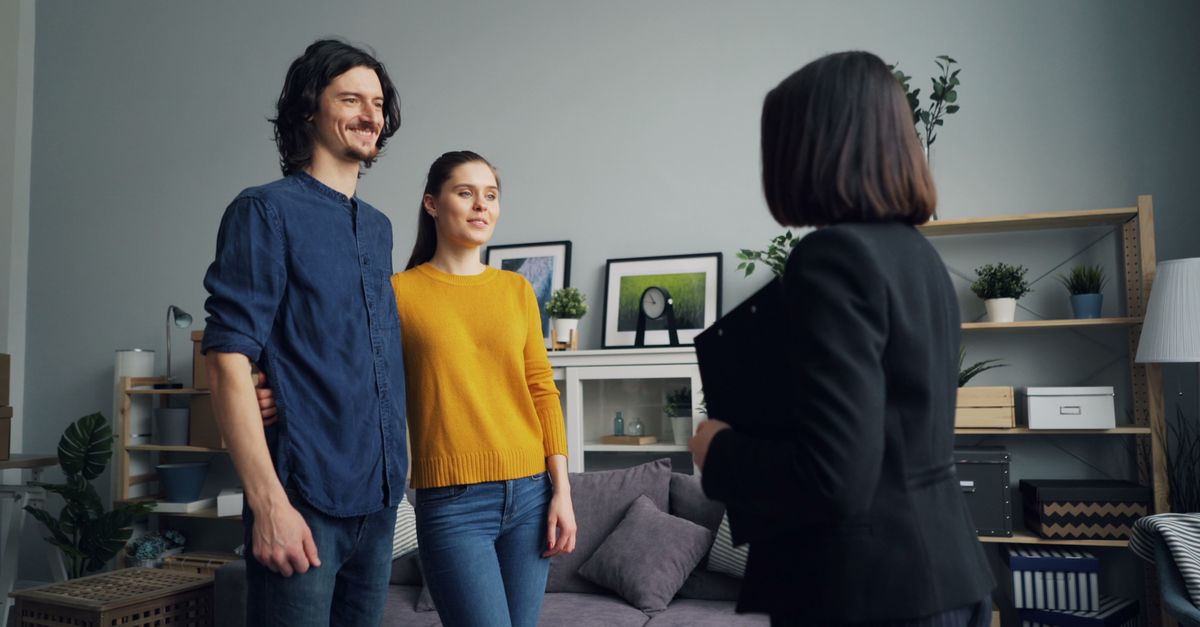 A smiling couple meets with a real estate agent in a stylish living room setting.
