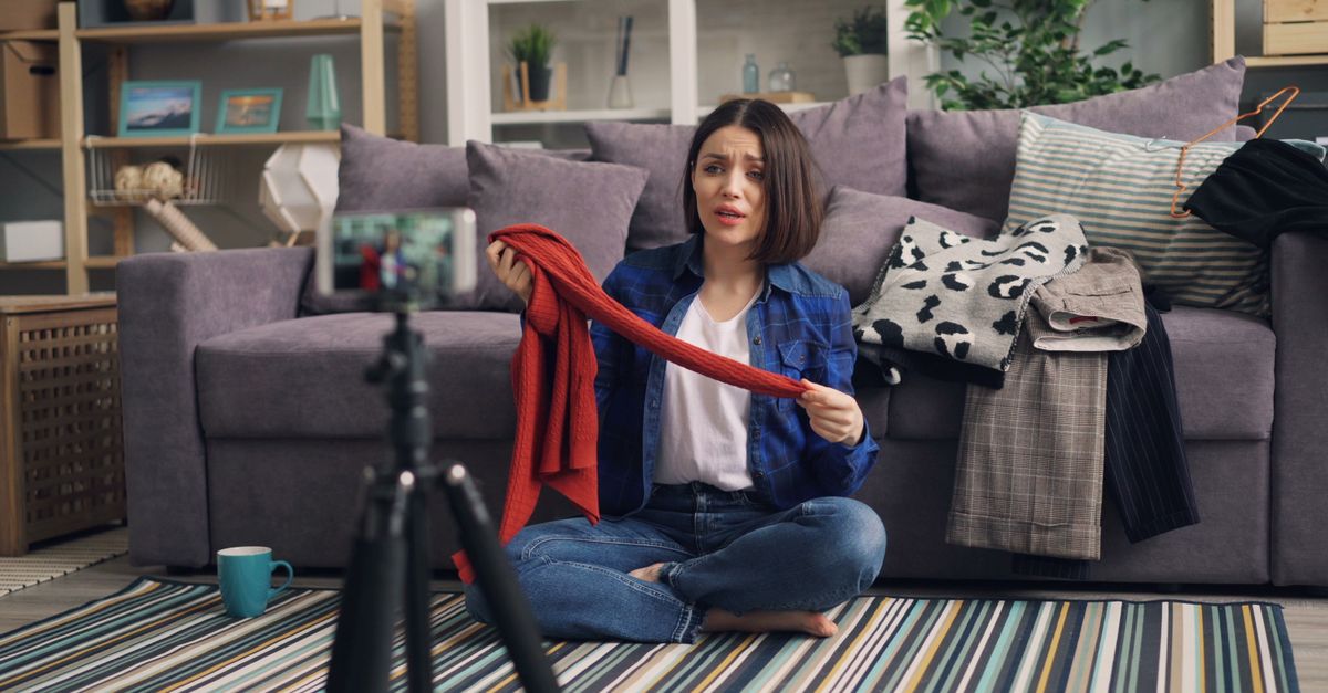 Woman recording a fashion vlog indoors, showcasing clothes in a cozy living room.