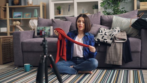 Woman recording a fashion vlog indoors, showcasing clothes in a cozy living room.