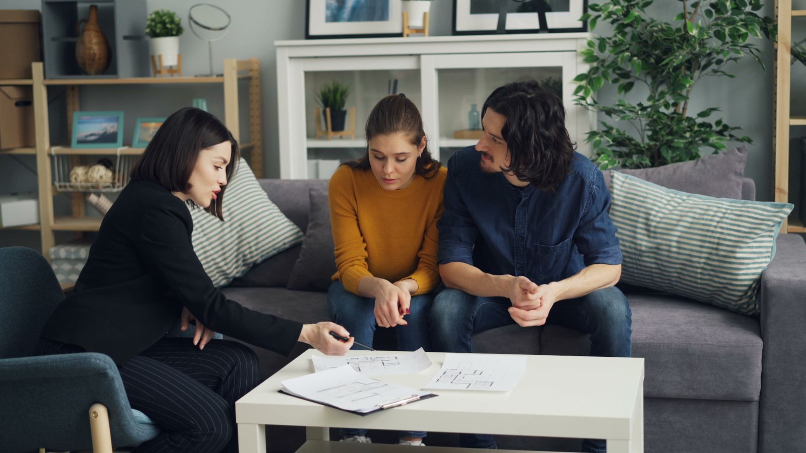A real estate agent discussing house plans with a couple in a living room.