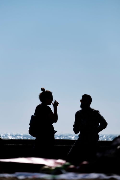Free Silhouette of a couple conversing by the Italian seashore under a clear sky. Stock Photo