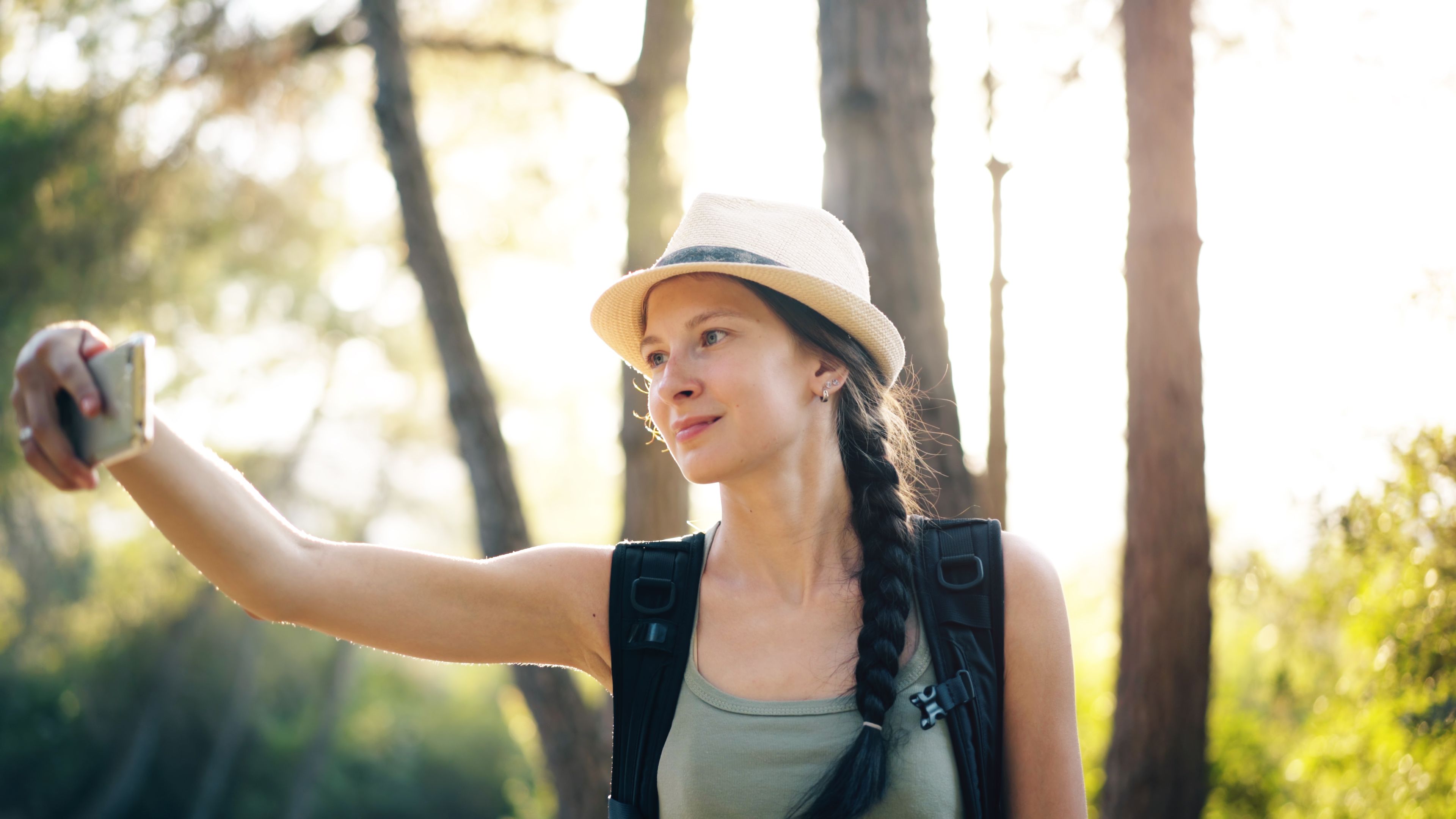 Hiker checking her phone among sunlit forest trees — photo by Vitaly Gariev on Pexels