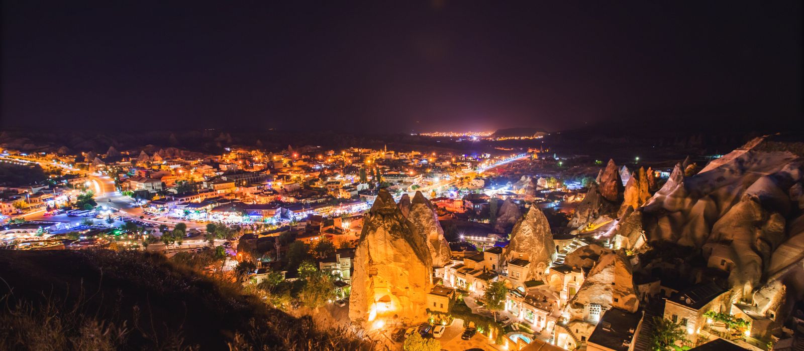 A vibrant nighttime aerial view of Göreme National Park with illuminated landmarks in Cappadocia, Turkey.