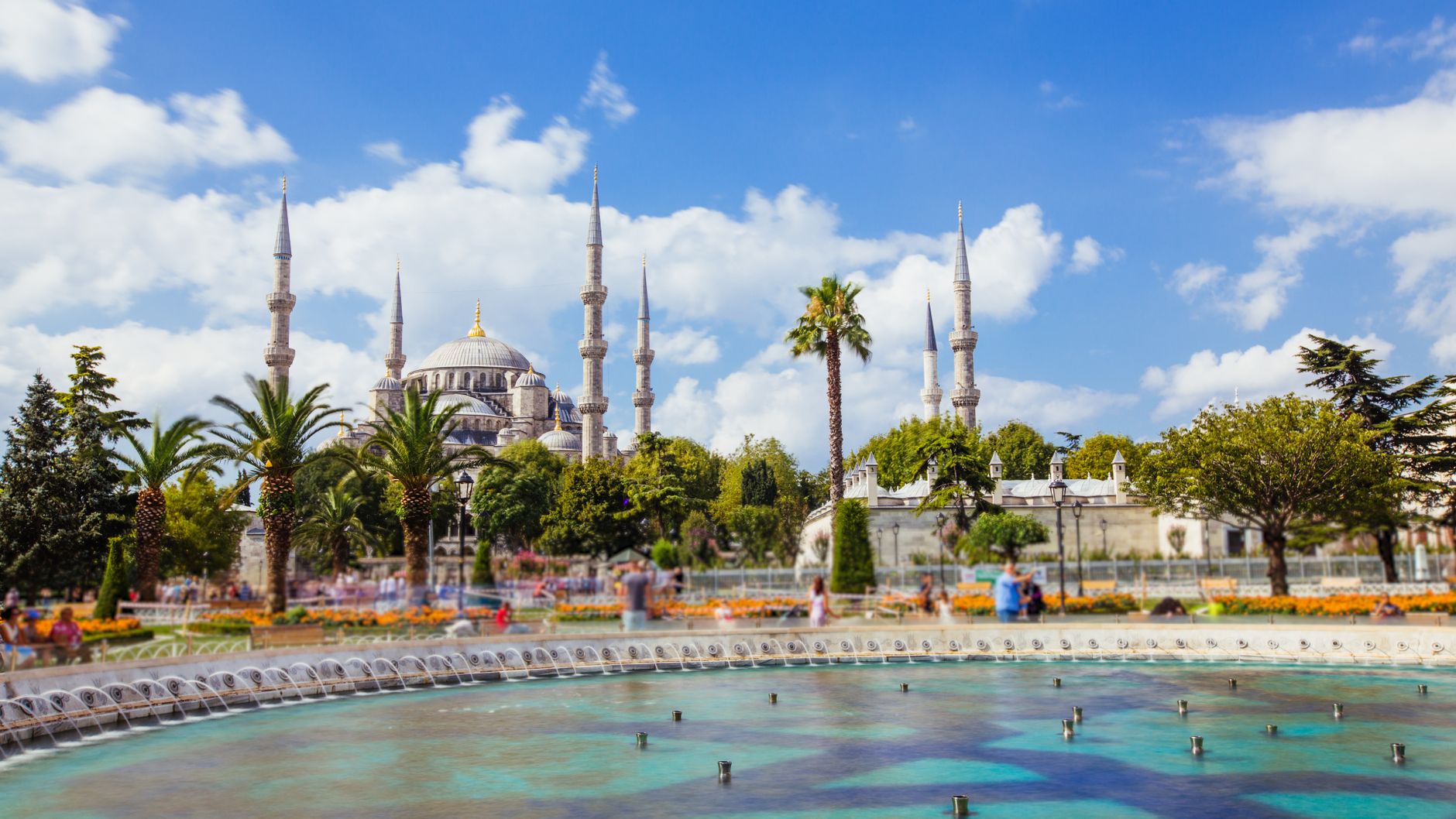 The iconic Blue Mosque and fountain viewed from a vibrant park in Istanbul, Turkey.