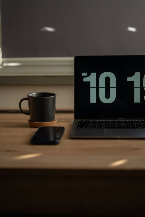 Free Cozy workspace setting with a laptop showing time, a mug, and a smartphone on a wooden desk. Stock Photo