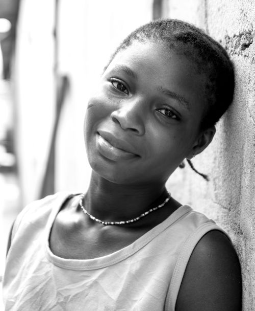 Free Black and white portrait of a smiling teenage girl with short hair and a necklace, leaning against a wall. Stock Photo