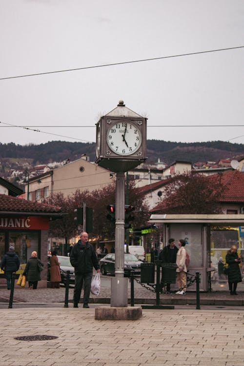 A clock on a street corner with people around it
