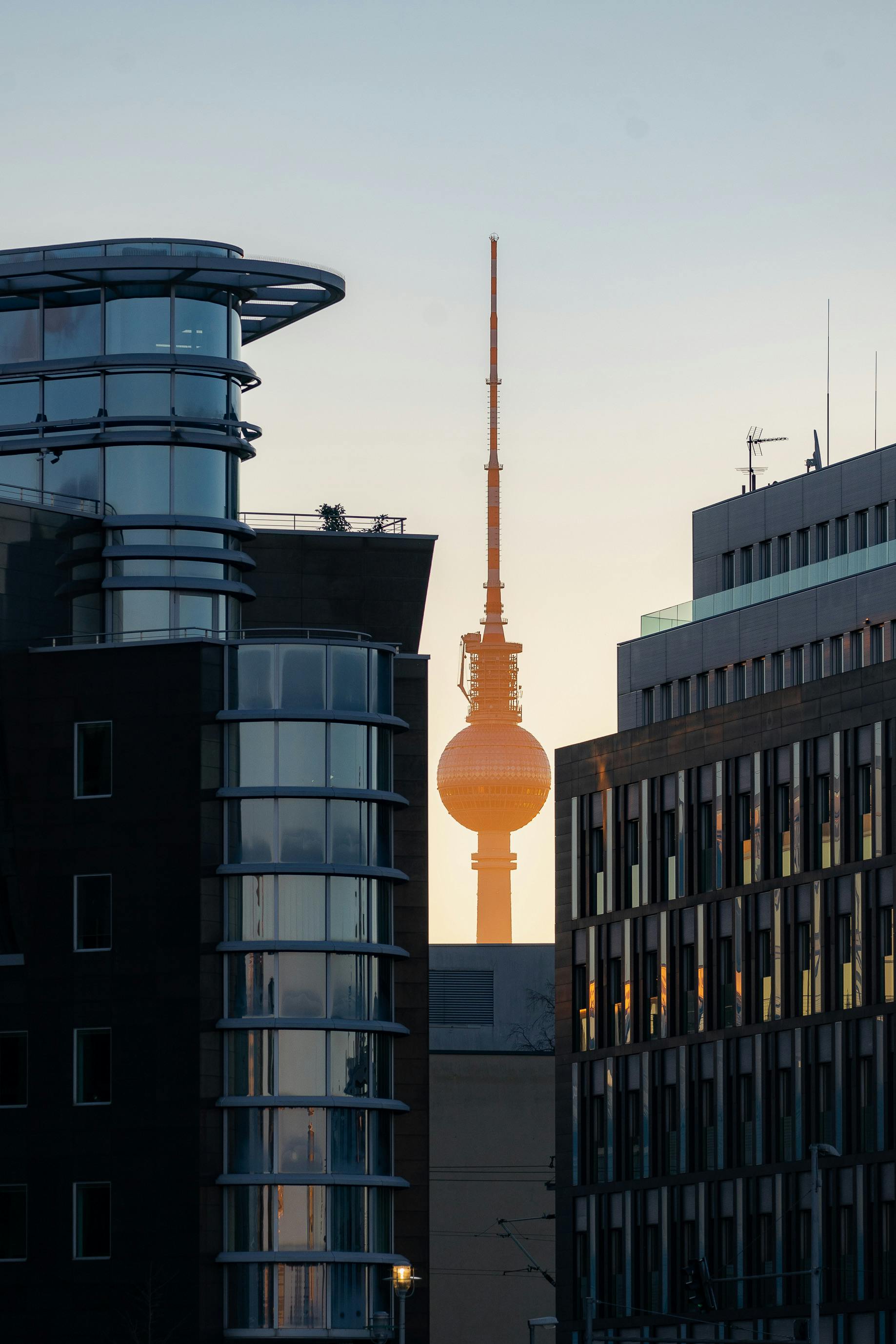 A sunset view of the Berlin TV Tower framed by contemporary city architecture, highlighting urban charm.