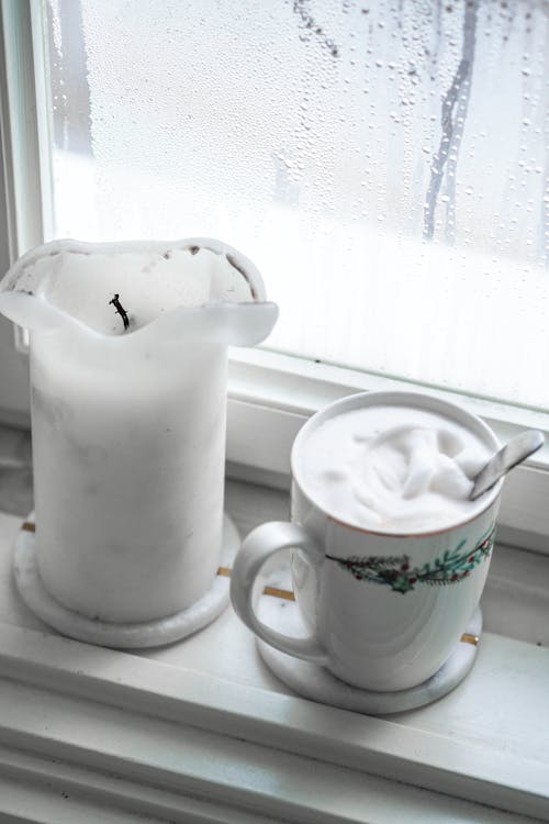 A white pitcher and a cup of coffee on a window sill