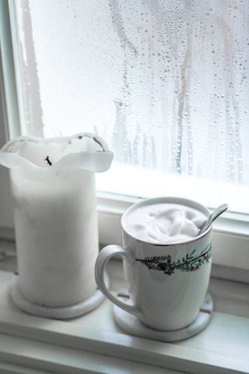 A cup of coffee and a candle sit on a window sill