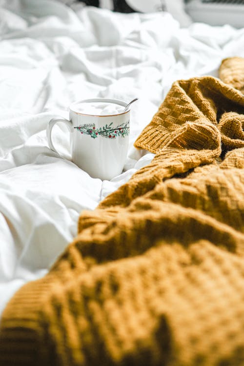 A cup of coffee on a bed with a blanket