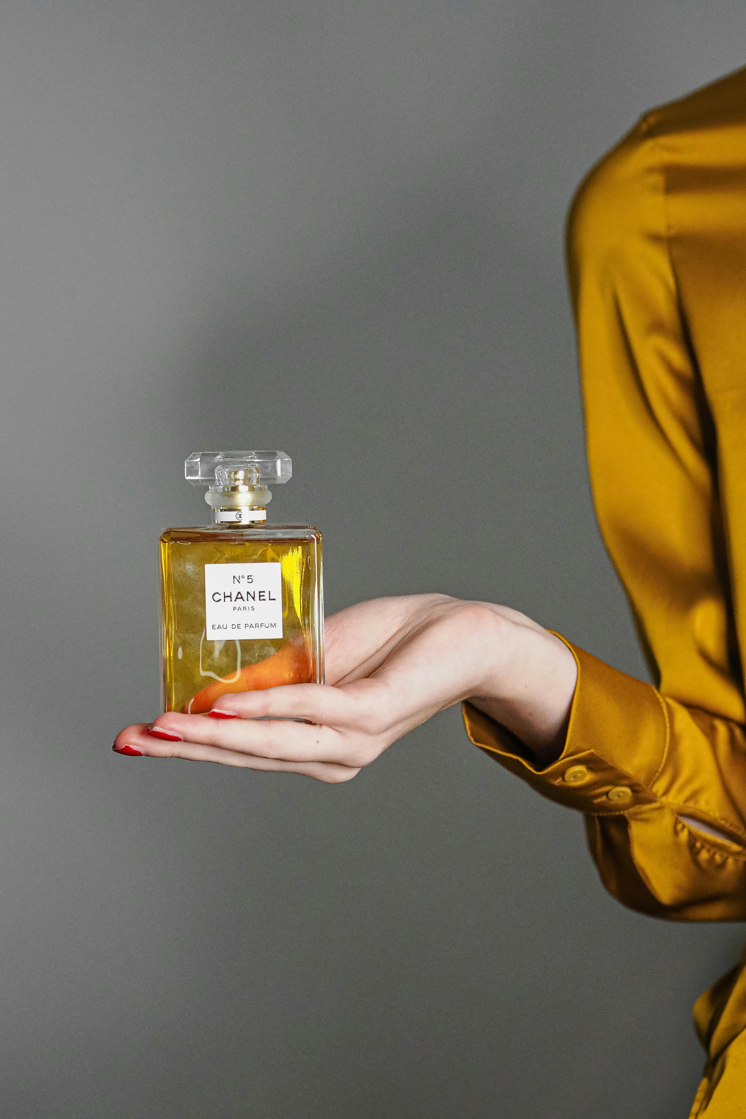 A hand elegantly holding a Chanel perfume bottle against a neutral background.