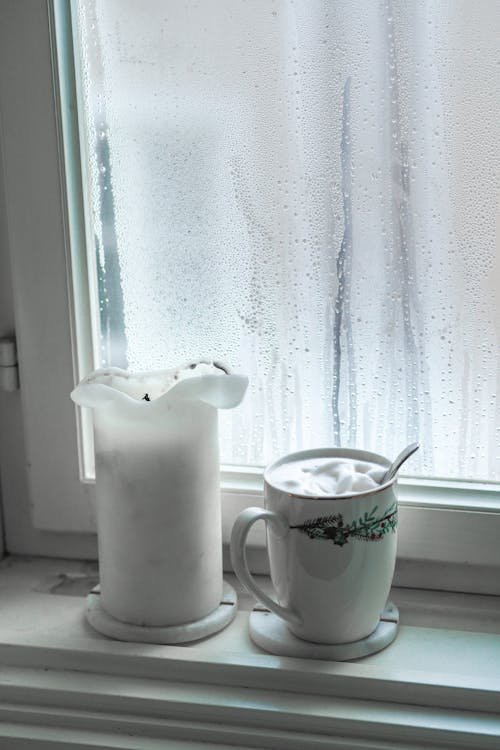 A cup of coffee and a candle sit on a window sill