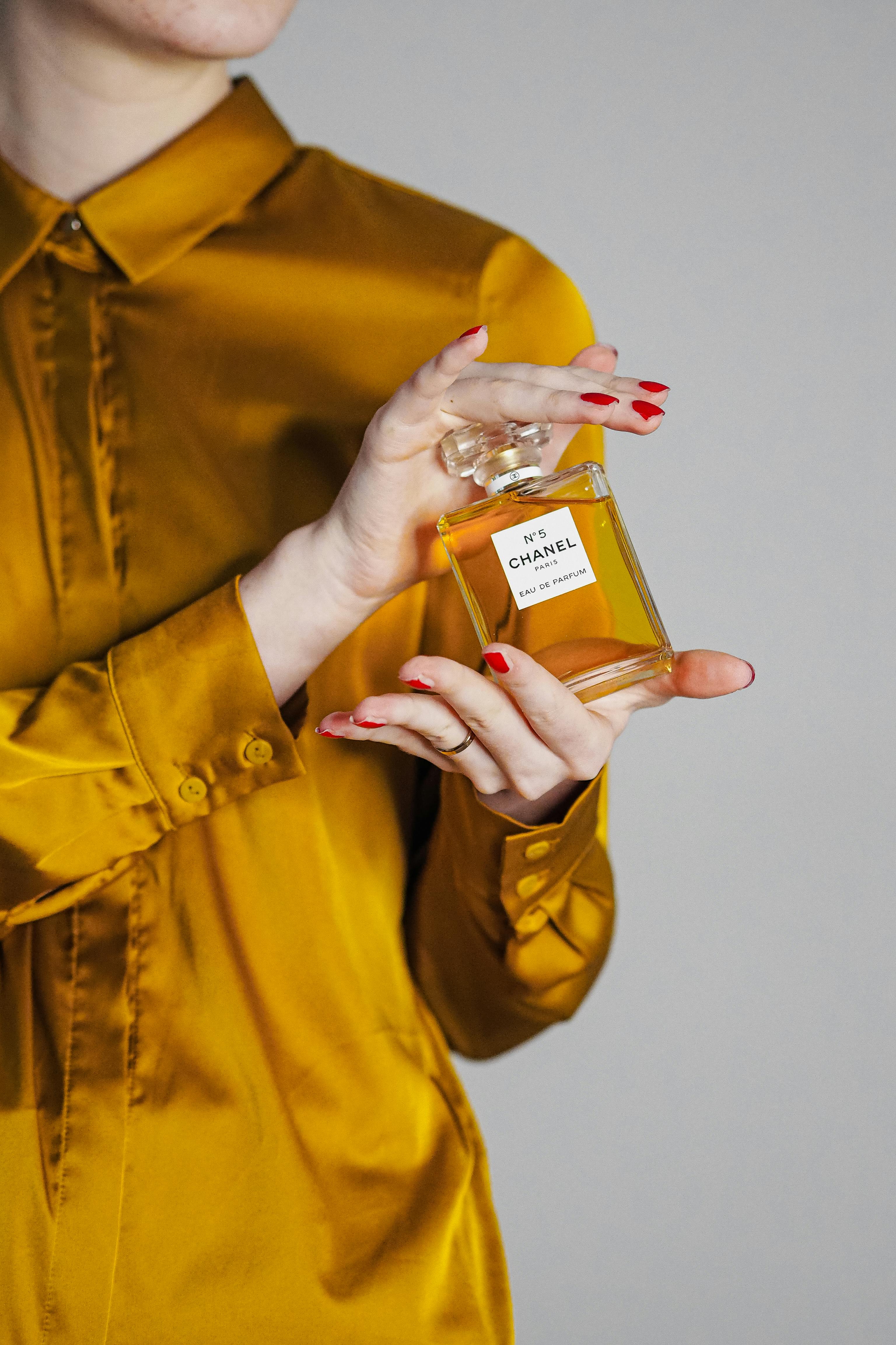 woman in a golden silk shirt holding a bottle of chanel no