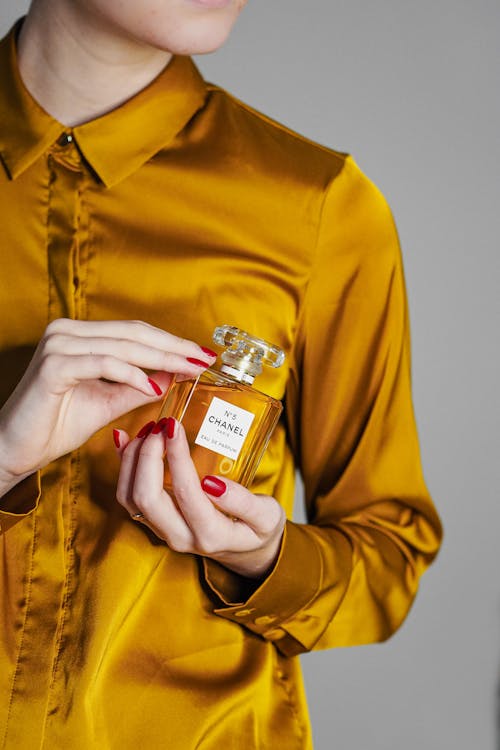 A woman in a yellow shirt holding a bottle of perfume