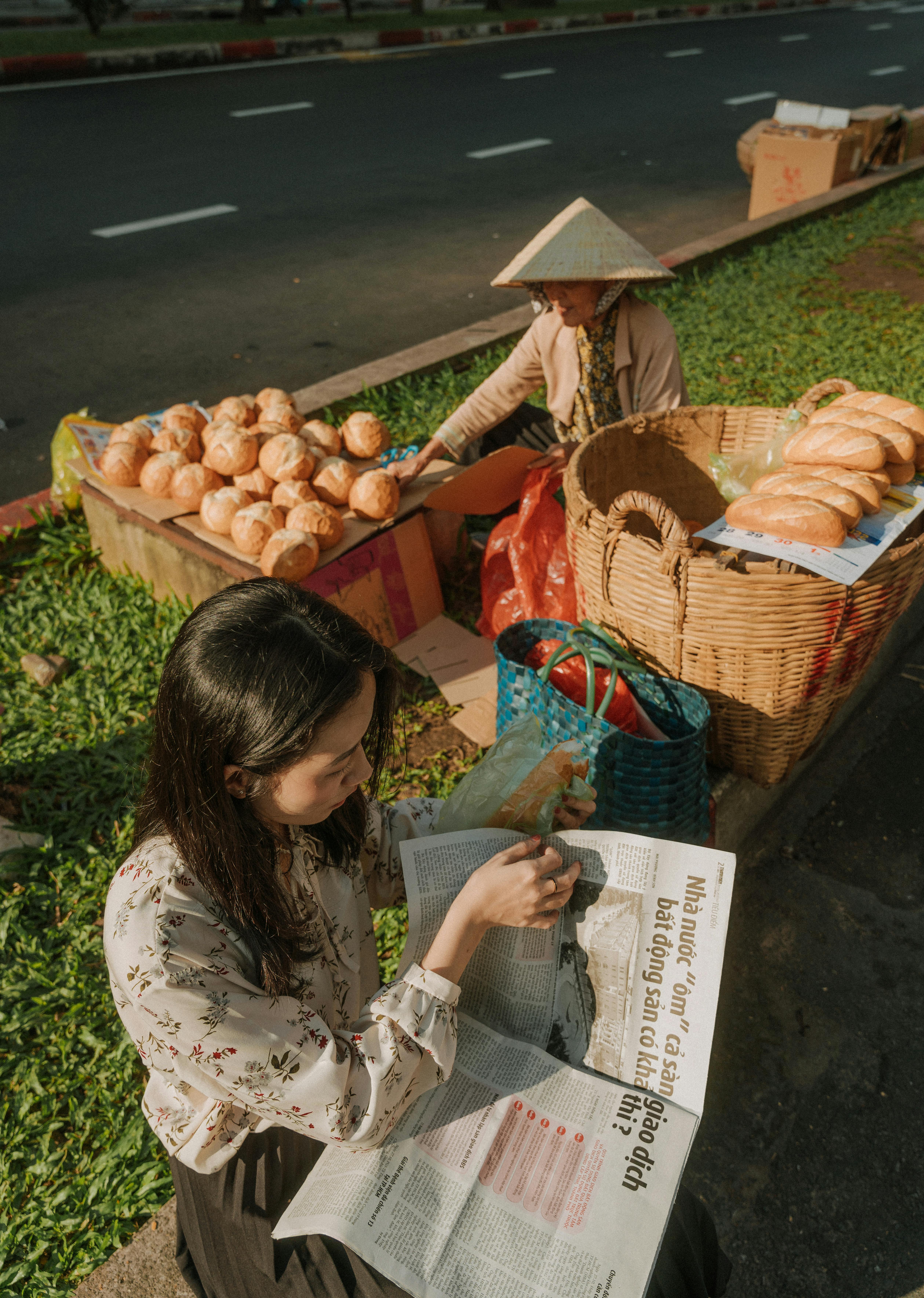 Asian women reading and selling bread by sidewalk in Ho Chi Minh City.