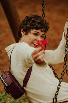 一位穿着毛衣的年轻女子，手持充满活力的红色花朵，在户外高兴地挥手