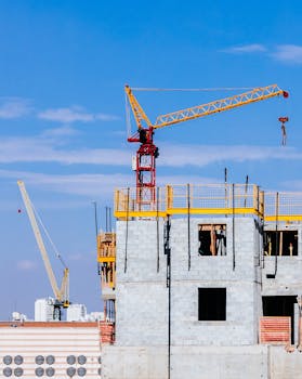 晴朗的蓝天下，建筑工地的塔式起重机正在高层建筑上作业