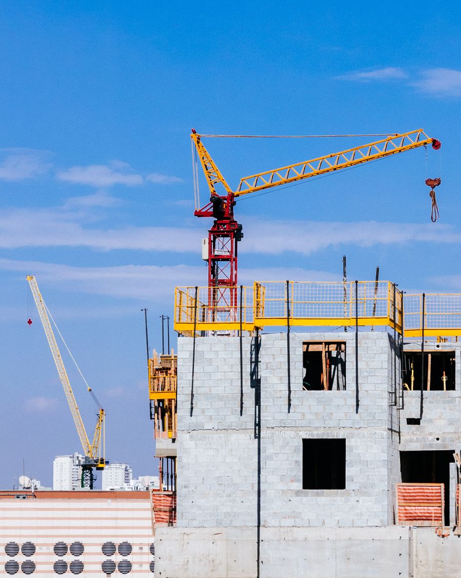 Red and yellow tower cranes atop a high-rise office tower under construction against clear blue sky - Cyberjaya Office Tower Fit-Out by Solidcraft Builders