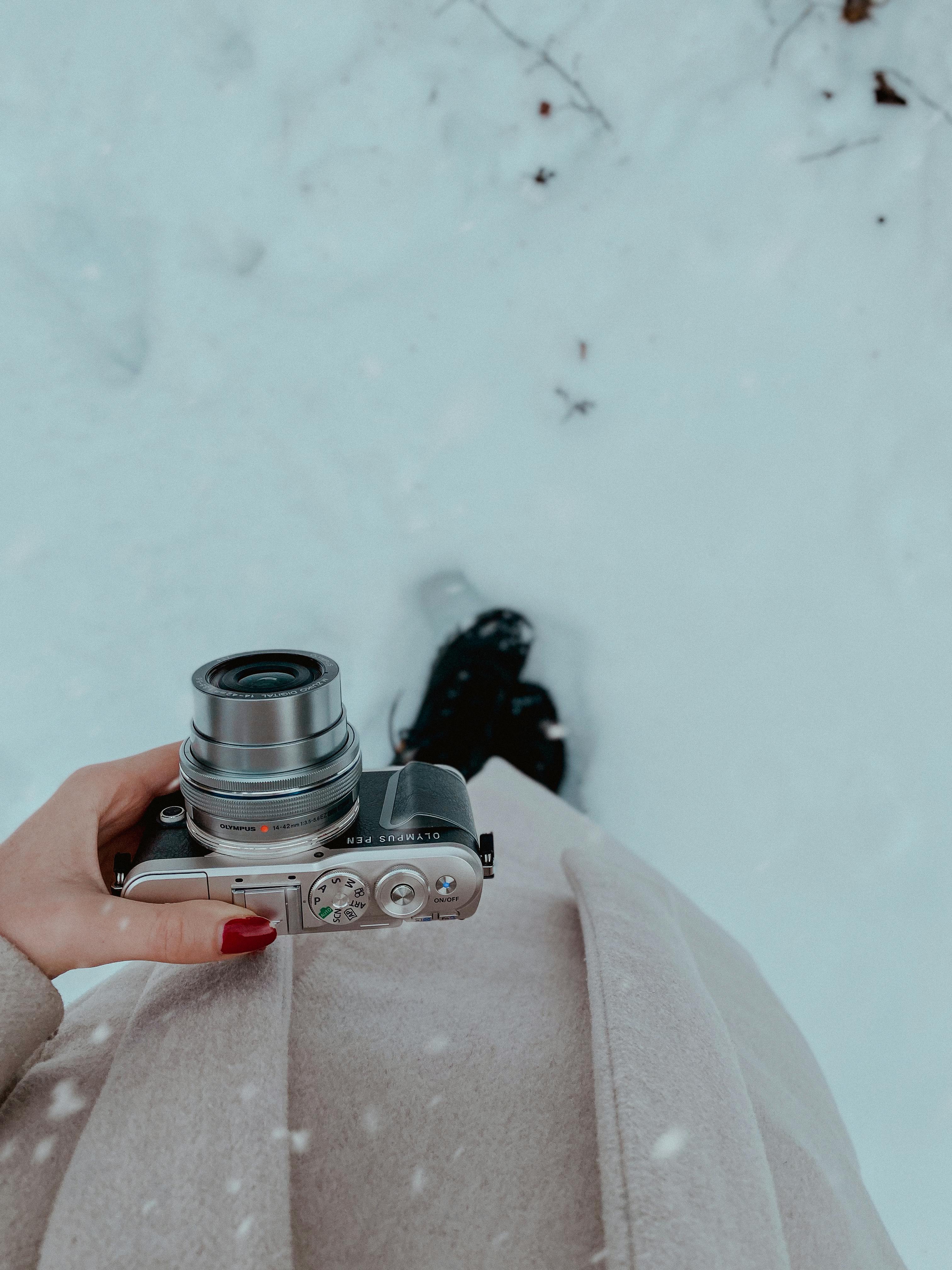Free A woman holding a camera captures a snowy winter moment outdoors. Stock Photo