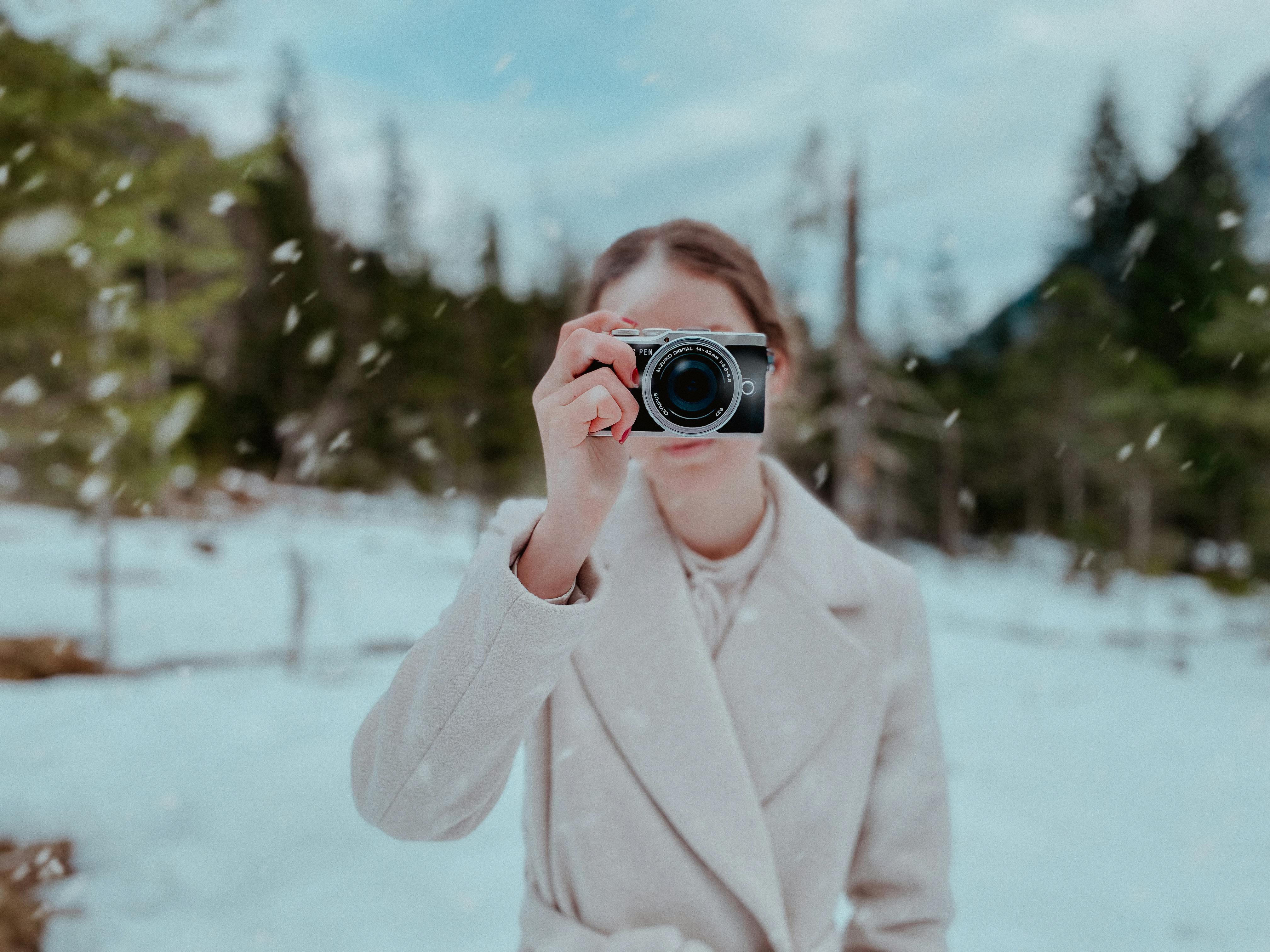 A woman photographing snowy countryside in winter, capturing nature's beauty.