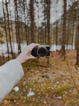 A hand holding a camera amidst a lush forest landscape in winter.
