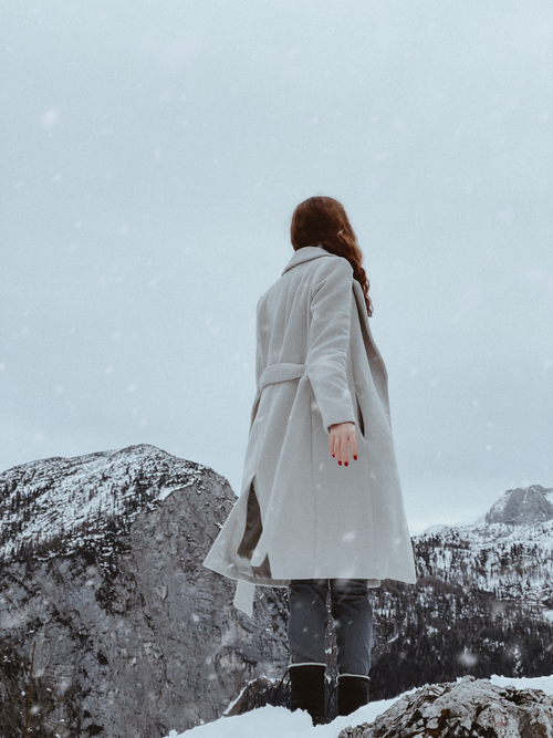 Free Woman in a grey coat standing in a snowy mountain landscape, evocative of winter serenity. Stock Photo