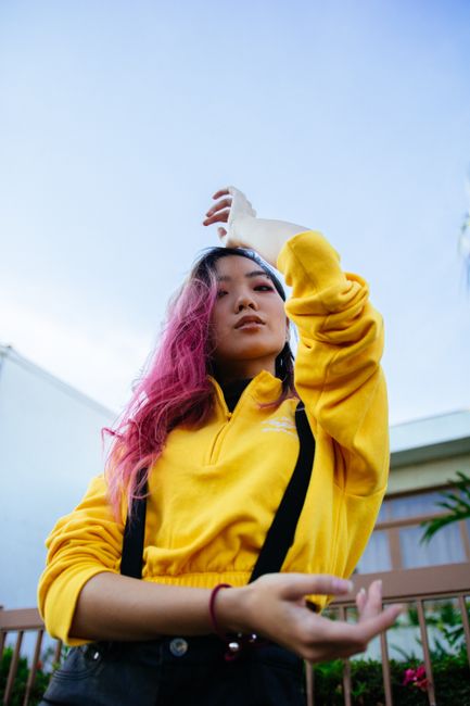 Fashionable young woman with pink hair posing outdoors in vibrant clothing.
