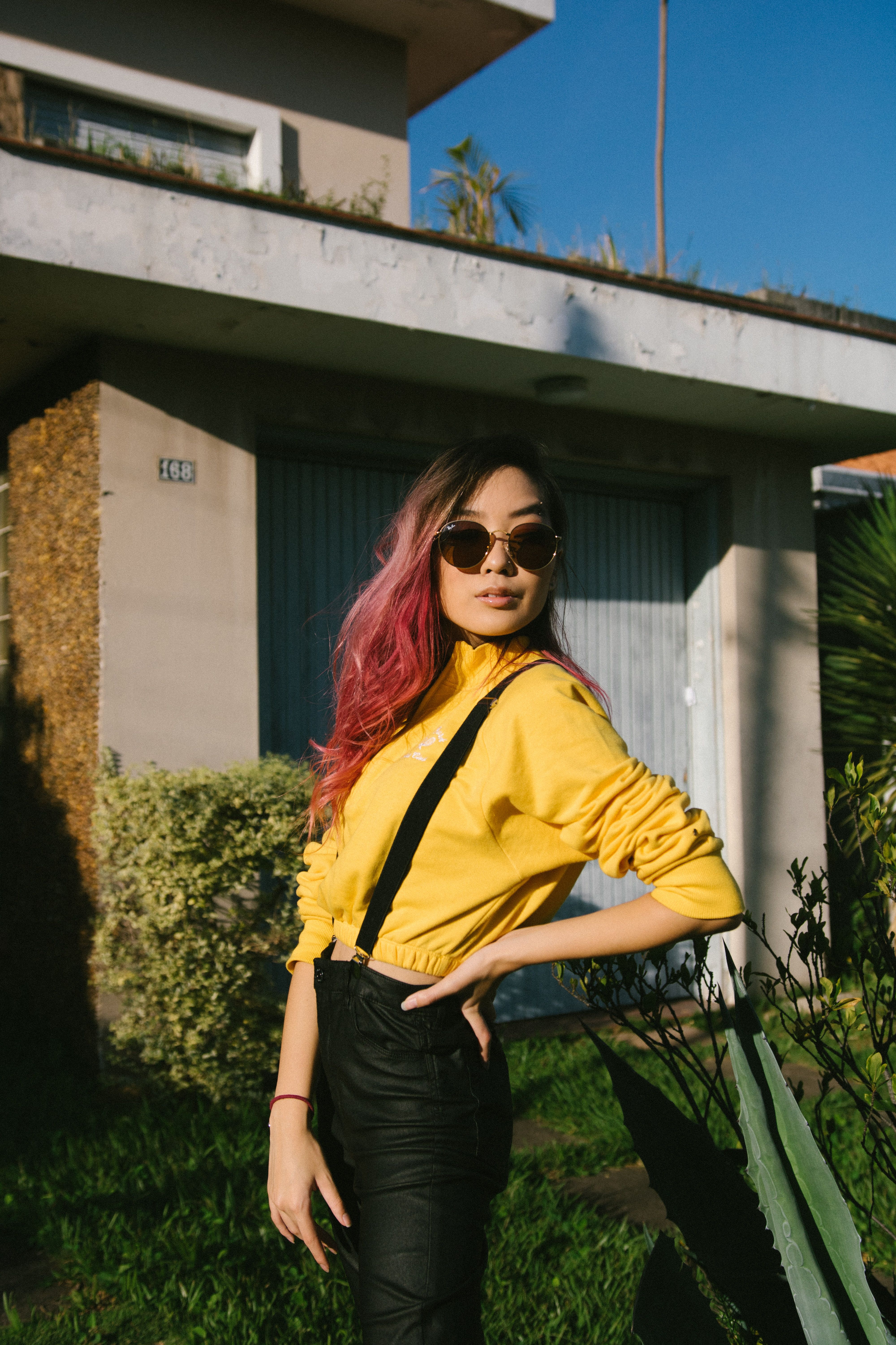 Stylish woman posing in a yard wearing a yellow top with sunglasses on a sunny day.