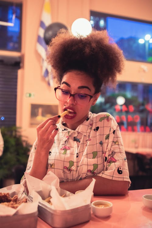 Woman in White and Green Shirt Eating Fries