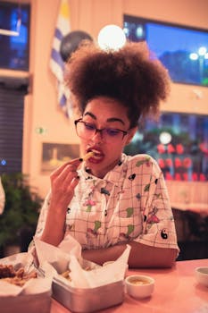 一位有着非洲式发型的女士戴着眼镜，在室内温馨、休闲的氛围中用餐