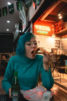 一位蓝发年轻女子在装饰充满活力的舒适餐厅里享用比萨