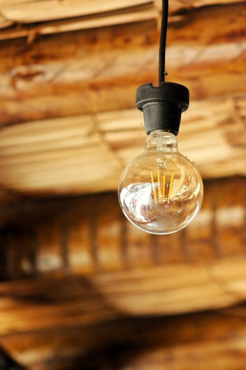 Free A close-up of a single light bulb hanging from a wooden ceiling. Stock Photo