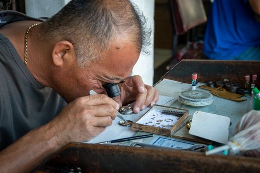 Close-up of a jeweler with a magnifying glass examining jewelry pieces passionately.