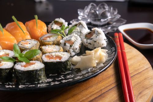 Free A mouth-watering assortment of sushi served with soy sauce, garnished with fresh herbs, and chopsticks on a wooden board. Stock Photo