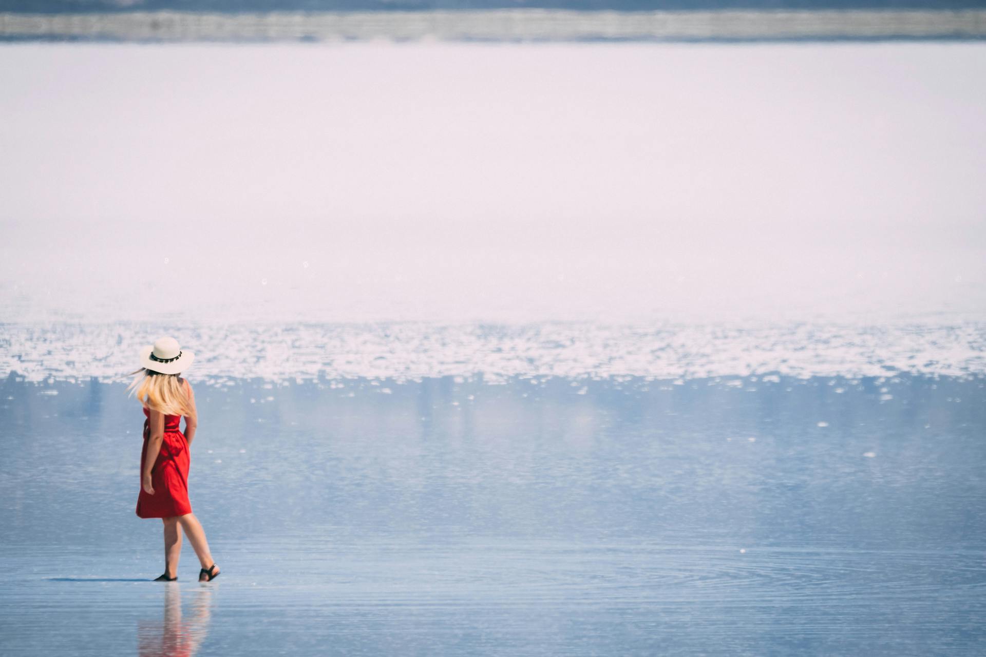 Elegant woman in a red dress walking on reflective Utah salt flats under daylight.