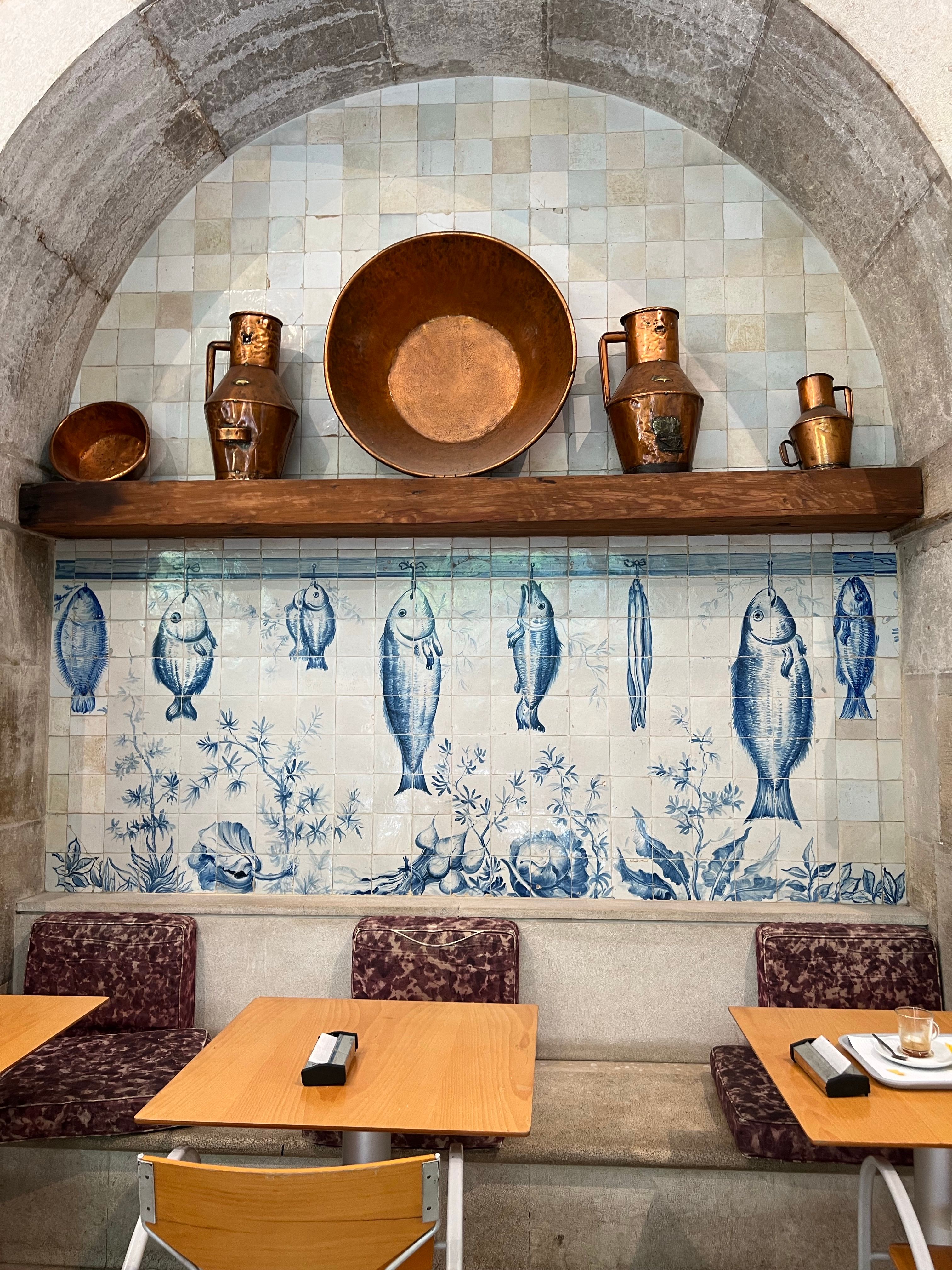 Panneau d'azulejos à poissons bleus et pichets en cuivre au-dessus d'une banquette