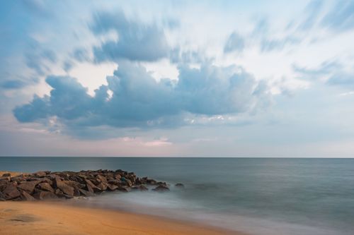 Free A tranquil seascape featuring a sandy beach, rocky shore, and dynamic cloud formations. Stock Photo