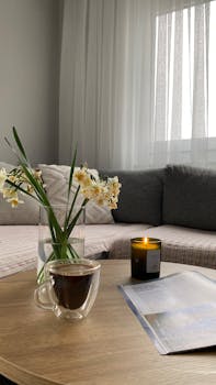 Warm and inviting living room with a coffee cup, candle, and a vase of flowers on a wooden table.