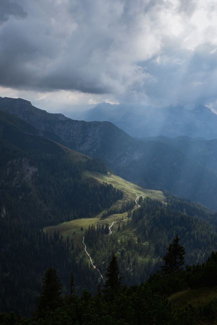 Captivating mountain scene with a winding path, fog, and sunlight breaking through the clouds.