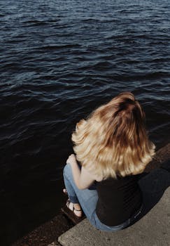 阳光明媚的日子里，一位金发女人穿着牛仔裤坐在水边