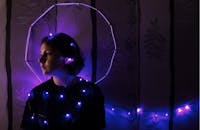 一名年轻女子在室内，借助紫色灯串的灯光，拍下了一幅情绪饱满的艺术肖像