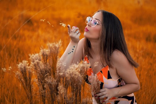 日落时分，一名有纹身的年轻女子在金色田野里吹着种子