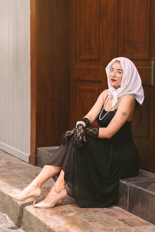 A woman in a black dress and white headscarf sitting on steps