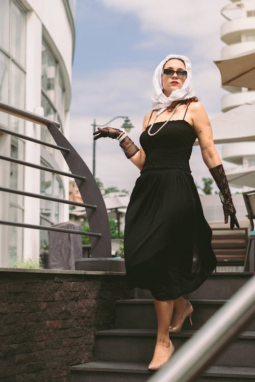 A woman in a black dress and sunglasses is walking down stairs