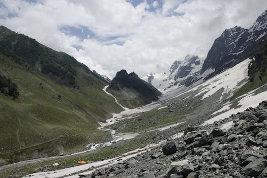Stunning mountain landscape with snow-capped peaks, a river, and lush greenery.