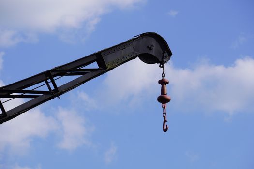 Close-up of an industrial crane arm with hook against a vibrant blue sky.