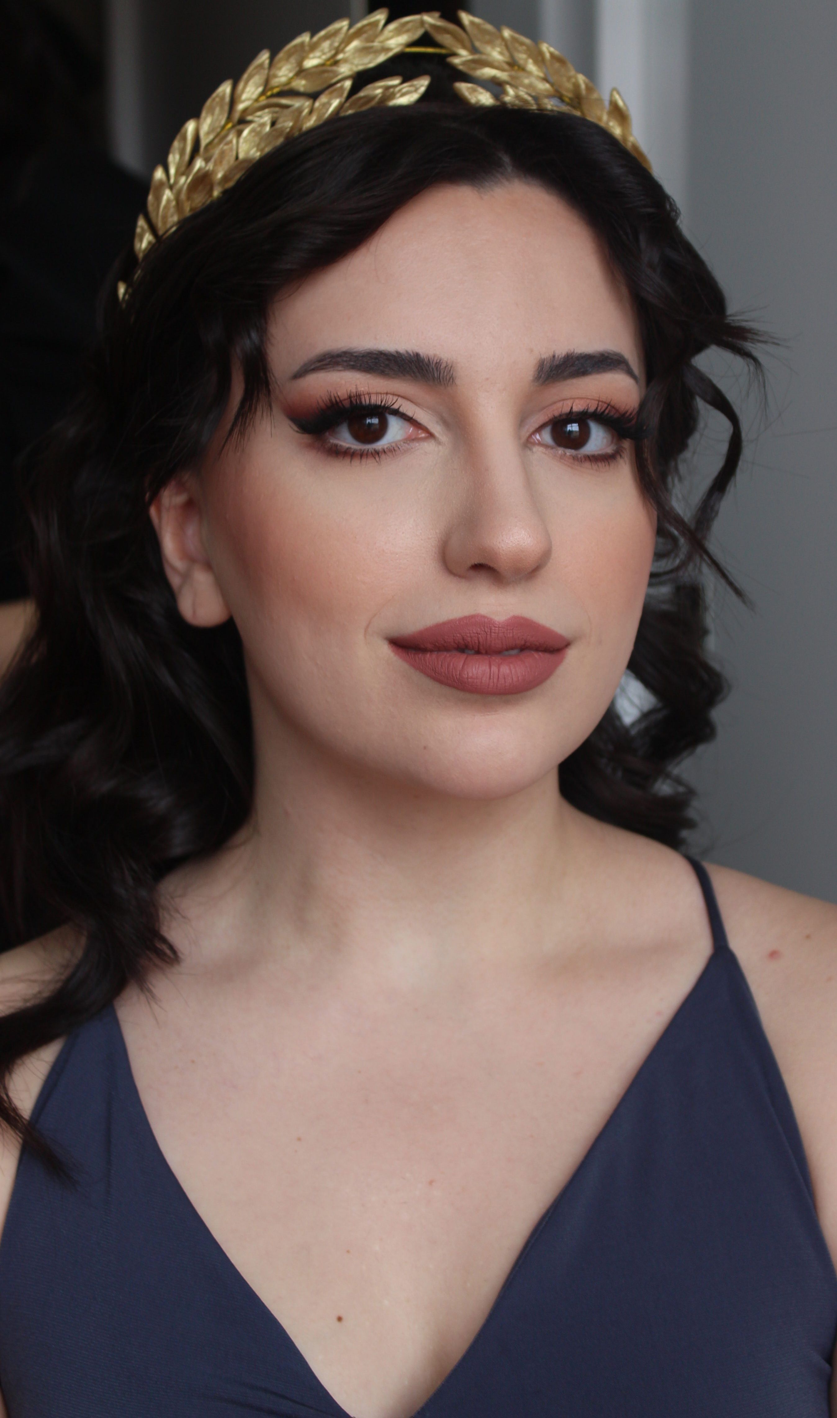 Close-up portrait of a beautiful brunette woman wearing a gold leaf crown, exuding glamour and elegance.