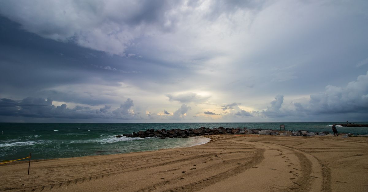Tranquil dawn view with dramatic clouds over a sandy beach and rocky coastline.